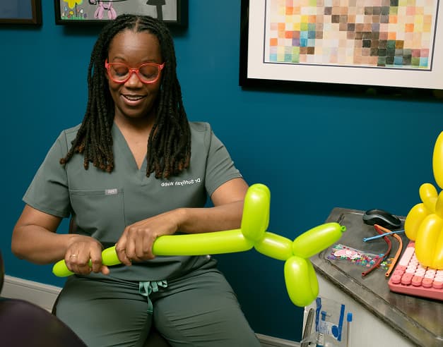 A person in scrubs making a green balloon animal.