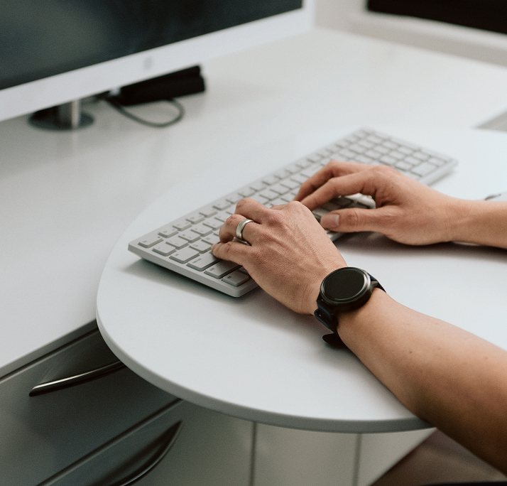 Hands typing on a sleek, white keyboard in a modern office setting. A smartwatch adorns one wrist, conveying a sense of productivity and focus.